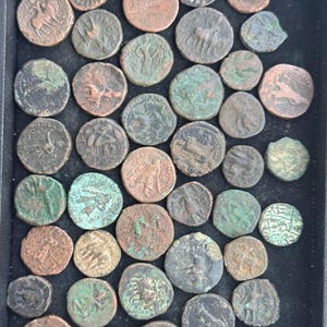 May include: A collection of antique bronze coins, each displaying intricate designs and varying degrees of wear. The coins are arranged in a black tray, showcasing their aged patina and historical significance. The coins have a mix of brown, green, and copper tones.