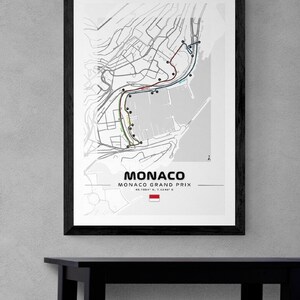 Peut inclure: Une carte en noir et blanc du circuit du Grand Prix de Monaco. La carte montre le parcours de la course, y compris les virages et la voie des stands. La carte indique &eacute;galement l'emplacement de la grille de d&eacute;part et de la ligne d'arriv&eacute;e. La carte est encadr&eacute;e d'un cadre noir et est accroch&eacute;e &agrave; un mur gris.
