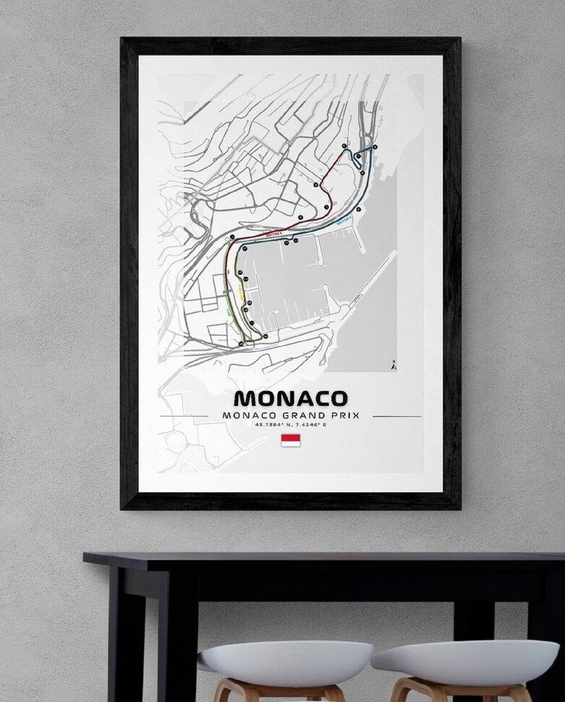 Peut inclure: Une carte en noir et blanc du circuit du Grand Prix de Monaco. La carte montre le parcours de la course, y compris les virages et la voie des stands. La carte indique &eacute;galement l'emplacement de la grille de d&eacute;part et de la ligne d'arriv&eacute;e. La carte est encadr&eacute;e d'un cadre noir et est accroch&eacute;e &agrave; un mur gris.