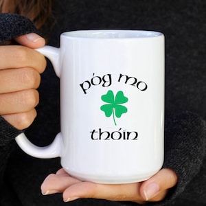 May include: White ceramic mug with a black shamrock and the text "póg mo thóin" in Irish Gaelic.