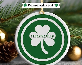 Könnte beinhalten: Weißer Keramik-Weihnachtsbaumschmuck mit einem grünen Kleeblatt und dem Wort "murphy" in keltischer Schrift. Der Schmuck ist von einem grünen Kreis mit weißem Rand umgeben.