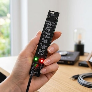 May include: A black modular synthesizer power supply unit panel featuring white printed mathematical physics formulas and symbols. The narrow vertical panel includes two small circular LED indicator lights, one glowing green and one glowing red, with a black power cable plugged into the bottom port.