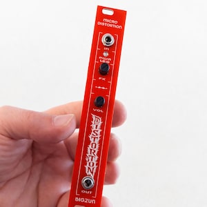 May include: A narrow, rectangular red modular synthesizer panel labeled Micro Distortion. It features a top input jack, a power LED, two black rotary knobs for FX and volume, and a bottom output jack. The text reads Distortion and BIG2UN.