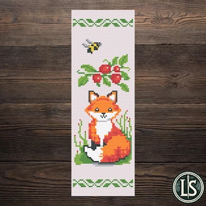 May include: A cross-stitch bookmark featuring a fox sitting in grass, with a bee and berries above. The fox is orange and white, with a black nose and eyes. The background is light pink, with green borders.