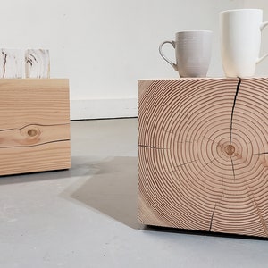 May include: Two wooden cube side tables with natural wood grain. One table has a visible knot and the other displays the tree's growth rings. Two mugs sit atop one table, and two decorative objects sit on the other.