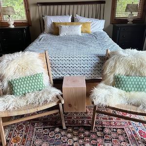 May include: Two white sheepskin chairs with green patterned cushions sit in front of a bed with a black and white patterned duvet. A wooden stool sits between the chairs on a red and black patterned rug.