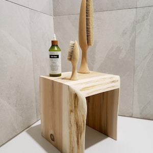 May include: A wooden stool with a natural wood finish. Two wooden hair brushes are on top of the stool, and a bottle of tea tree and mint hair rinse is in front of the brushes.