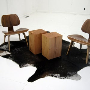 May include: Two wooden chairs with a black and white cowhide rug and two wooden square stools in a white room.