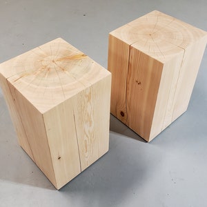 May include: Two natural wood square stools with a light wood finish. The top of each stool has a circular grain pattern.