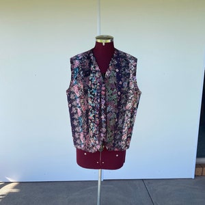 May include: A floral patterned waistcoat with a zip fastening. The waistcoat is displayed on a mannequin on a tripod stand.