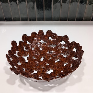 May include: A decorative brown bowl with a floral design. The bowl is made of metal and has a glossy finish. The bowl is sitting on a white surface.
