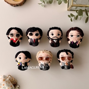 Puede incluir: Una colección de siete muñecos de ganchillo hechos a mano, cada uno representando a una persona con peinados, gafas y atuendos únicos. Los muñecos son de varios colores, incluyendo negro, marrón y beige, y están dispuestos sobre una superficie clara. El texto "LAMAGURUMI" es visible.