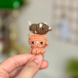 Op de afbeelding: Een kleine gehaakte oranje kat met zwarte ogen en een bruin-witte gehaakte muis op zijn kop.