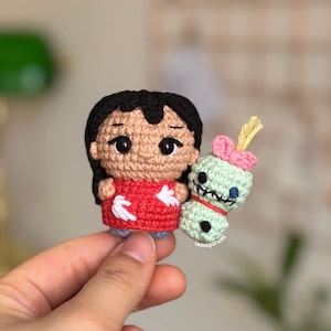 Könnte beinhalten: Handgefertigte Amigurumi-Figuren aus Häkelarbeit. Eine ist eine Figur in einem roten Kleid mit schwarzen Haaren, die andere ein grüner Außerirdischer mit einer rosa Schleife. Die Figuren sind detailliert, mit sichtbaren Stichen und Gesichtszügen. Der Außerirdische hat ein rotes Band und den Text "tamagurumi".