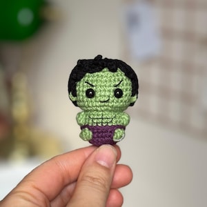 Könnte beinhalten: Eine kleine gehäkelte grüne Hulk-Figur mit einer lila Windel. Die Figur hat schwarze Haare und einen süßen Ausdruck.