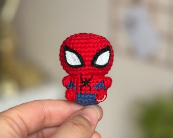 Może przedstawiać: Mała pluszowa zabawka amigurumi Spider-Mana wykonana na szydełku. Zabawka jest czerwona i niebieska z czarnym wzorem pająka na klatce piersiowej. Zabawka ma białe oczy i czarny obrys.
