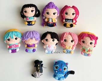 May include: A collection of ten colorful, crocheted dolls with various hairstyles and outfits. The dolls have detailed facial features and are arranged in two rows. One doll is a blue tiger, and another is a black and gray creature.