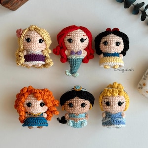 以下が含まれることがあります： 6体の手作りの編みぐるみ人形のコレクション。それぞれ異なるプリンセスを表しています。人形は、赤、金髪、黒、オレンジの髪など、さまざまな色の詳細な糸細工が施されており、象徴的な衣装を着ています。人形の高さは約7.6cmです。