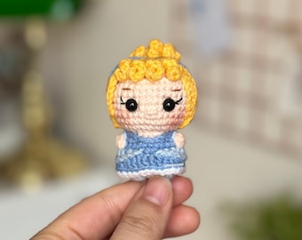 May include: A crocheted doll with yellow hair, blue eyes, and a blue dress. The doll is wearing a white crown.