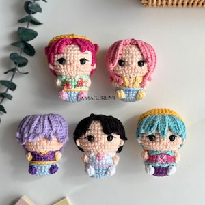 Può includere: Sei bambole amigurumi fatte a mano con vari colori di capelli, tra cui rosa, viola, nero e blu. Ogni bambola ha un outfit unico, con dettagli come motivi floreali e colori contrastanti. Le bambole sono all'uncinetto e presentano il testo "LAMAGURUMI".