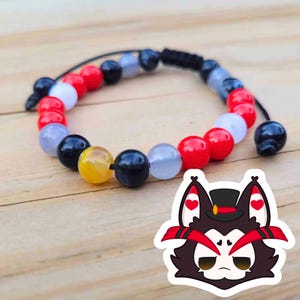 May include: A beaded bracelet featuring a variety of colorful beads in red, white, black, yellow, and blue. The bracelet is strung on a black cord with adjustable knots. A sticker of a cartoon wolf is in the bottom right corner.