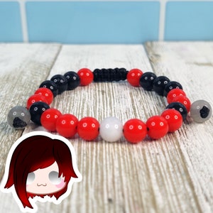 May include: A beaded bracelet featuring red, black, and white round beads. The bracelet is strung on a black cord and has a macrame closure. The beads are approximately 0.4 inches in diameter. The bracelet is displayed on a light wood surface.
