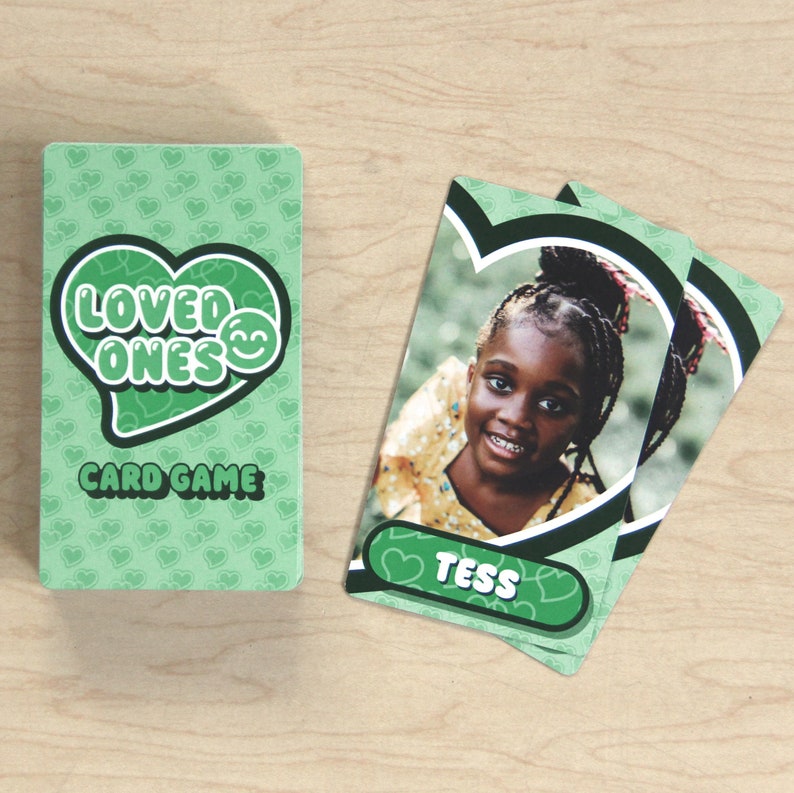 Puede incluir: Juego de cartas verde con las palabras "Loved Ones" y un dise&ntilde;o de coraz&oacute;n. La carta presenta una foto de una ni&ntilde;a con el nombre "Tess" impreso debajo.