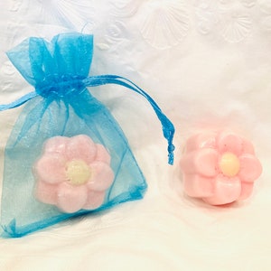 May include: Two pink flower-shaped soaps, one in a blue organza bag. The soaps have a raised flower design with a yellow center.