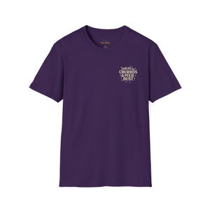 Puede incluir: Camiseta morada de manga corta con la frase "Fueled by Churros & Pixie Dust" en una fuente caprichosa. Tiene cuello redondo y parece estar hecha de un tejido suave.