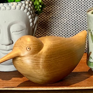 Könnte beinhalten: Eine Holzvogelskulptur mit hellbrauner Oberfläche. Der Vogel hat einen langen Schnabel und einen runden Körper.