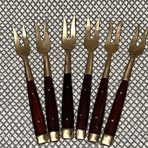 Op de afbeelding: Set van zes gouden cocktailvorken met donkerbruine houten handvatten.