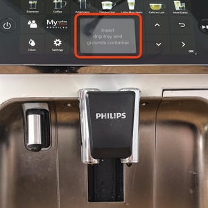 May include: A close-up of a Philips espresso machine. The machine's display shows the text "Insert drip tray and grounds container." The machine has a black and silver design with various coffee drink options displayed.