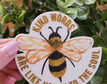 May include: A white sticker with a bee illustration and the text "Kind words are like honey to the soul". The text is in gold lettering and the bee is yellow and black.