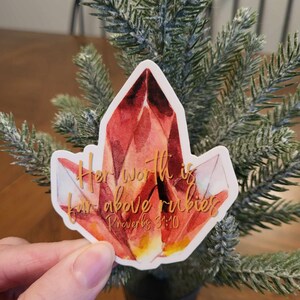 May include: A red crystal sticker with gold lettering that reads "Her worth is far above rubies Proverbs 31:10".