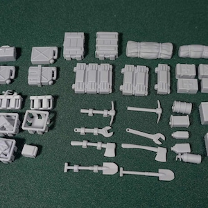 Puede incluir: Una colección de kits de maquetas de plástico gris para un diorama militar. Los kits incluyen diversos suministros militares, herramientas y equipos, como cajas, barriles, palas, hachas y un pico.