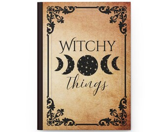 Op de afbeelding: Een notitieboek met harde kaft, een beige achtergrond in perkamentstijl en een zwarte, sierlijke rand. De kaft bevat de tekst "WITCHY THINGS" in zwarte letters, gescheiden door een centrale afbeelding van drie maanfasen met sterren en manen.