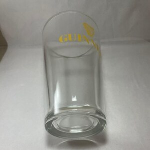 May include: A clear pint glass with the word "GUINNESS" printed in yellow. The glass has a cylindrical shape with a slightly flared top and a thick, rounded base. The Guinness logo is visible.