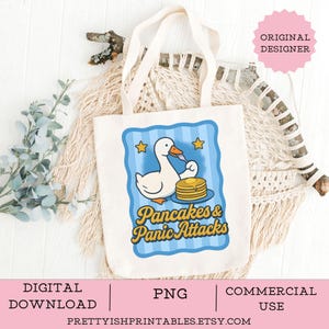 May include: A cream-colored tote bag featuring a cartoon duck eating pancakes. The duck is inside a blue frame with yellow stars. The text "Pancakes & Panic Attacks" is in yellow and brown. The words "Digital Download", "PNG", and "Commercial Use" are at the bottom.