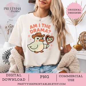 Könnte beinhalten: Cremefarbenes T-Shirt mit einer Cartoon-Ente, die einen Cowboyhut trägt und einen herzförmigen Spiegel hält. Der Text "AM I THE DRAMA?" ist über der Ente aufgedruckt. Das Design enthält rosa Sterne und die Wörter "DIGITALER DOWNLOAD", "PNG" und "KOMMERZIELLE NUTZUNG".