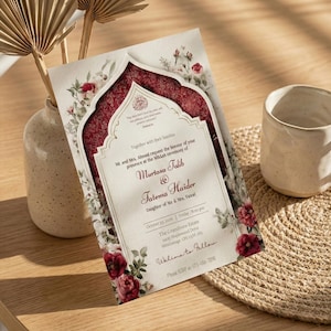Puede incluir: Una invitaci&oacute;n de boda con un dise&ntilde;o floral burdeos y blanco. La invitaci&oacute;n presenta los nombres Murtasa Talib y Fatema Haider. La invitaci&oacute;n est&aacute; sobre una mesa de madera con una taza beige y un salvamanteles tejido.