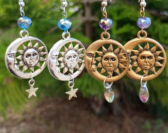 May include: Four pairs of celestial-themed earrings. Two pairs are silver-toned with a sun and moon design, a star charm, and blue beads. The other two pairs are gold-toned with a sun and moon design, a teardrop charm, and purple beads.