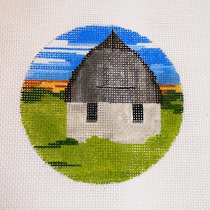 May include: A round needlepoint ornament featuring a white barn with a gray roof against a green field and blue sky.