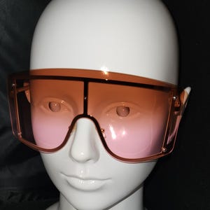 May include: A pair of oversized sunglasses with a brown frame and pink gradient lenses.