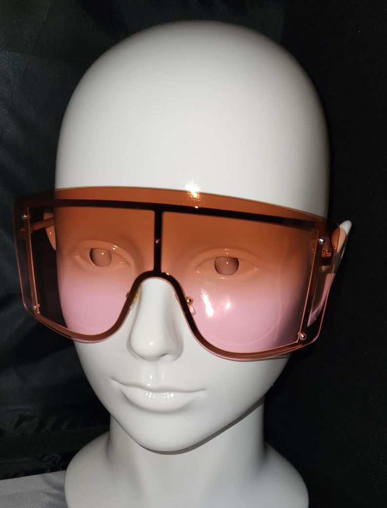 May include: A pair of oversized sunglasses with a brown frame and pink gradient lenses.