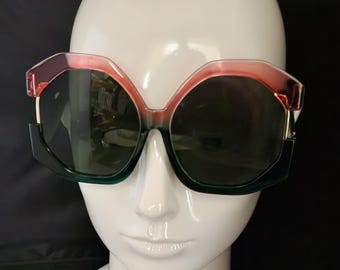 May include: Oversized sunglasses with a green and pink frame. The lenses are dark green.