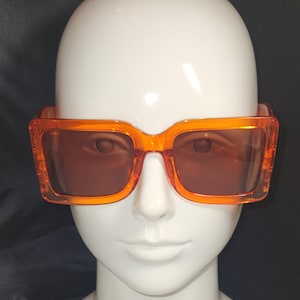 May include: Orange square-shaped sunglasses with brown lenses.