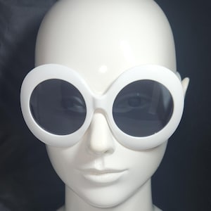 Könnte beinhalten: Weiße runde Sonnenbrille mit schwarzen Gläsern. Die Sonnenbrille sitzt auf einem weißen Mannequin-Kopf.