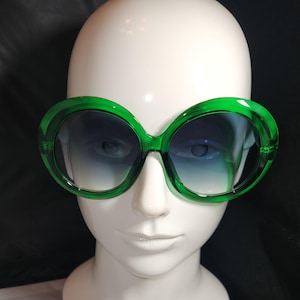 Puede incluir: Gafas de sol redondas de gran tamaño con montura verde y lentes azules degradados.