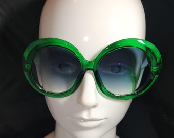 May include: Green oversized round sunglasses with a blue gradient lens.