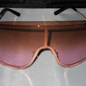 May include: Oversized sunglasses with a gradient pink lens and a black frame.